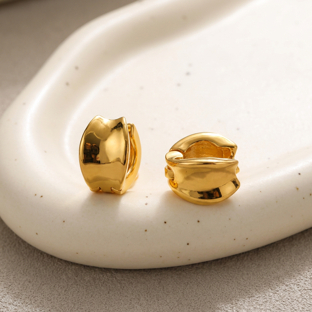 Sienna sculptural gold-plated hoop earrings on a warm ivory ceramic dish